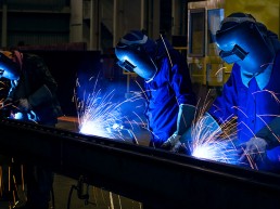 Bright orange sparks fly as workers weld metal in a factory.